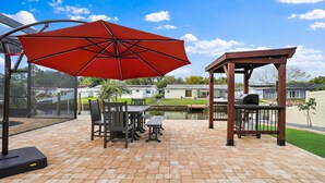 A patio area with a red umbrella, a wooden pergola, and a grill station.