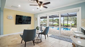 A spacious patio with a pool, a ceiling fan, and a television mounted on the wall.