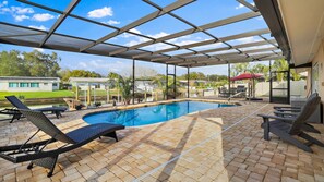 Une piscine extérieure couverte, dotée de chaises longues, d’un espace barbecue et offrant une vue sur un quartier résidentiel.