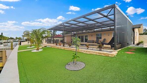 Une maison moderne dotée d’un espace extérieur couvert, d’une piscine et d’une pelouse bien entretenue.