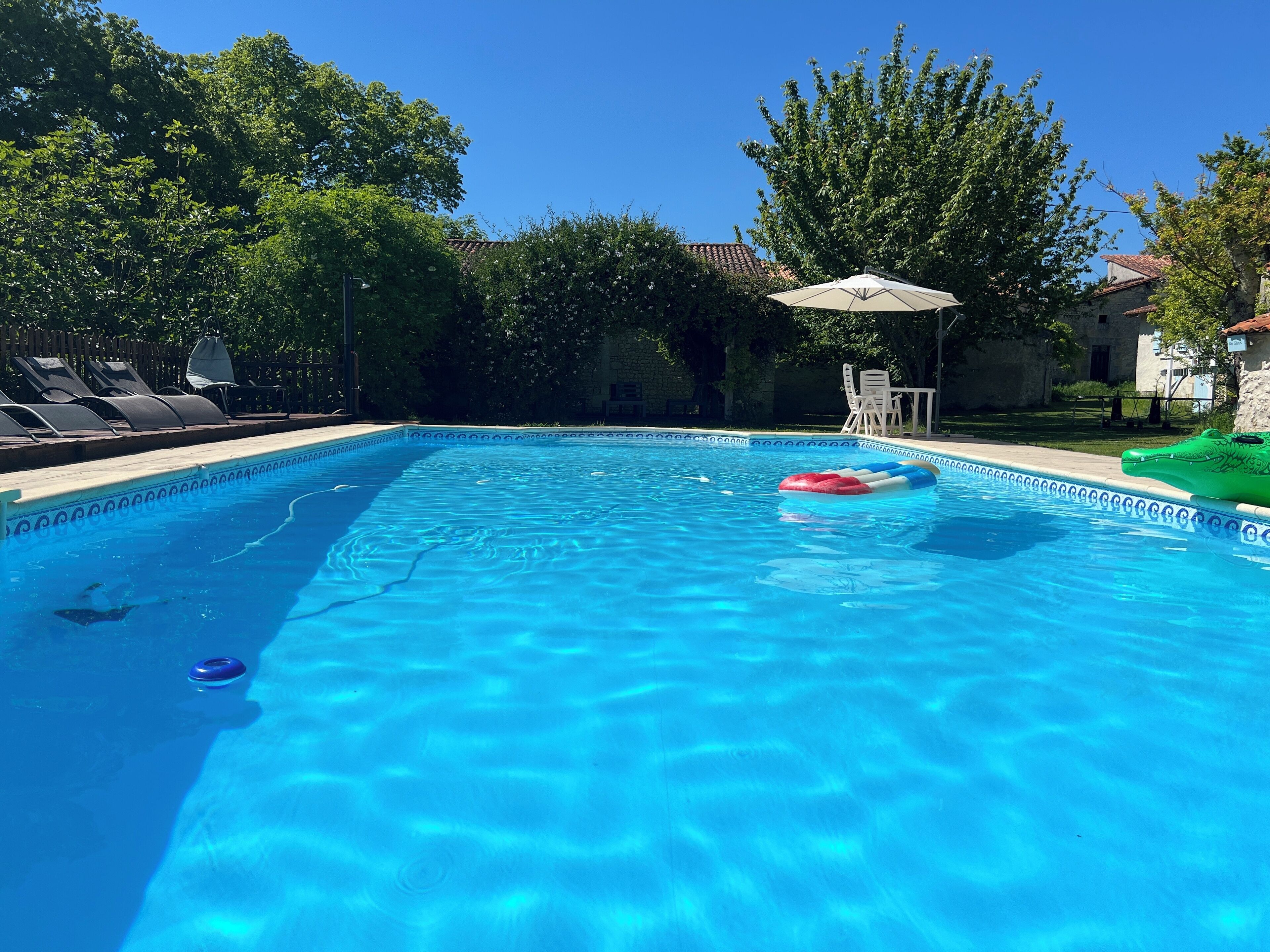 En klarblå pool med en flytande badring, omgiven av solstolar och en uteplats.
