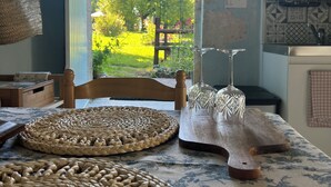 A kitchen with a view of a garden, a wooden chair, and a woven placemat on the table. - Entire Cosy cottage with pool idyllic location close to Aubeterre AMAZING VALUE! (Saint-Romain)