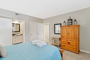 Une chambre à coucher comprenant un lit, une armoire en bois, une coiffeuse avec un miroir et une porte donnant sur une autre pièce.