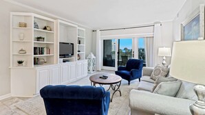 Un salón espacioso con un mueble blanco grande para entretenimiento, un televisor de pantalla plana y un balcón con vistas.