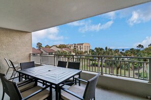 A balcony with a table and chairs, overlooking a residential area with palm trees and houses.