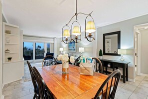 A dining area with a wooden table, chairs, a vase with flowers, and a chandelier.