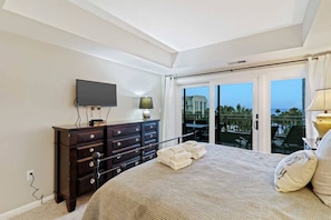Une chambre à coucher avec un lit, une commode, une télévision et un balcon offrant une vue.