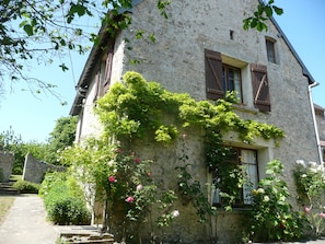 Ein mit Efeu und Rosen bewachsenes Steinhaus, mit Fenster und Tür.