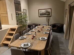 Ein Esszimmer mit einem langen Holztisch, der für eine Mahlzeit gedeckt ist, umgeben von Ledersofas und einer Treppe.