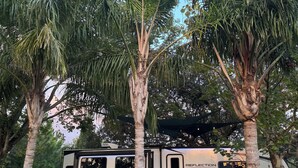 A recreational vehicle with a covered outdoor seating area, a fire pit, and a view of surrounding trees.
