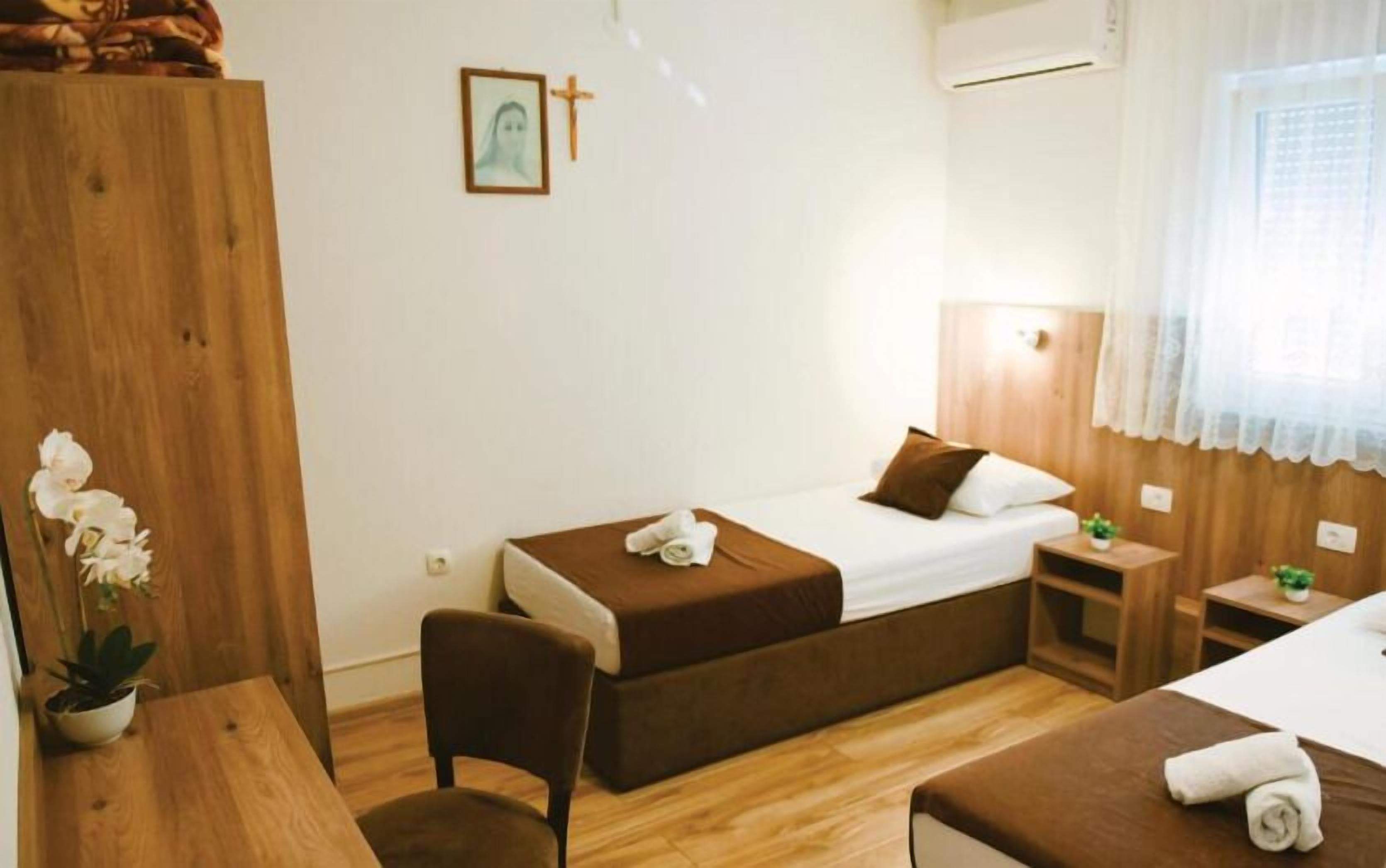 Habitación de hotel con dos camas, un armario de madera, una mesita con una planta y un aire acondicionado de pared.
