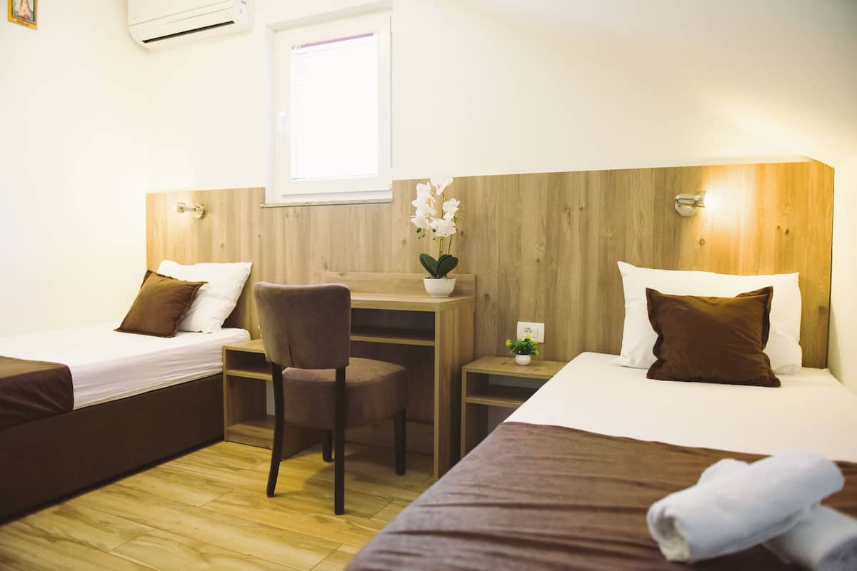A hotel room with two single beds, a wooden desk, a chair, and a small table with a plant.