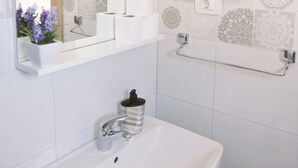 Une salle de bain avec un lavabo blanc, un miroir, un sèche-cheveux et un porte-serviettes.