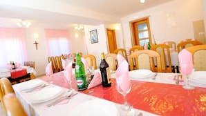 Un espace repas avec des tables dressées pour accueillir plusieurs convives, agrémenté d’une nappe rouge, de assiettes, de couverts et de verres disposés avec soin.