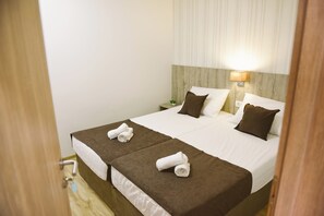 A double bed with brown and white bedding, a nightstand with a lamp, and a small plant. - Mica Medjugorje (Citluk)