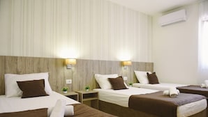 Une chambre d’hôtel avec deux lits simples, une tête de lit en bois, une petite table de chevet avec une lampe et un appareil de climatisation fixé au mur.
