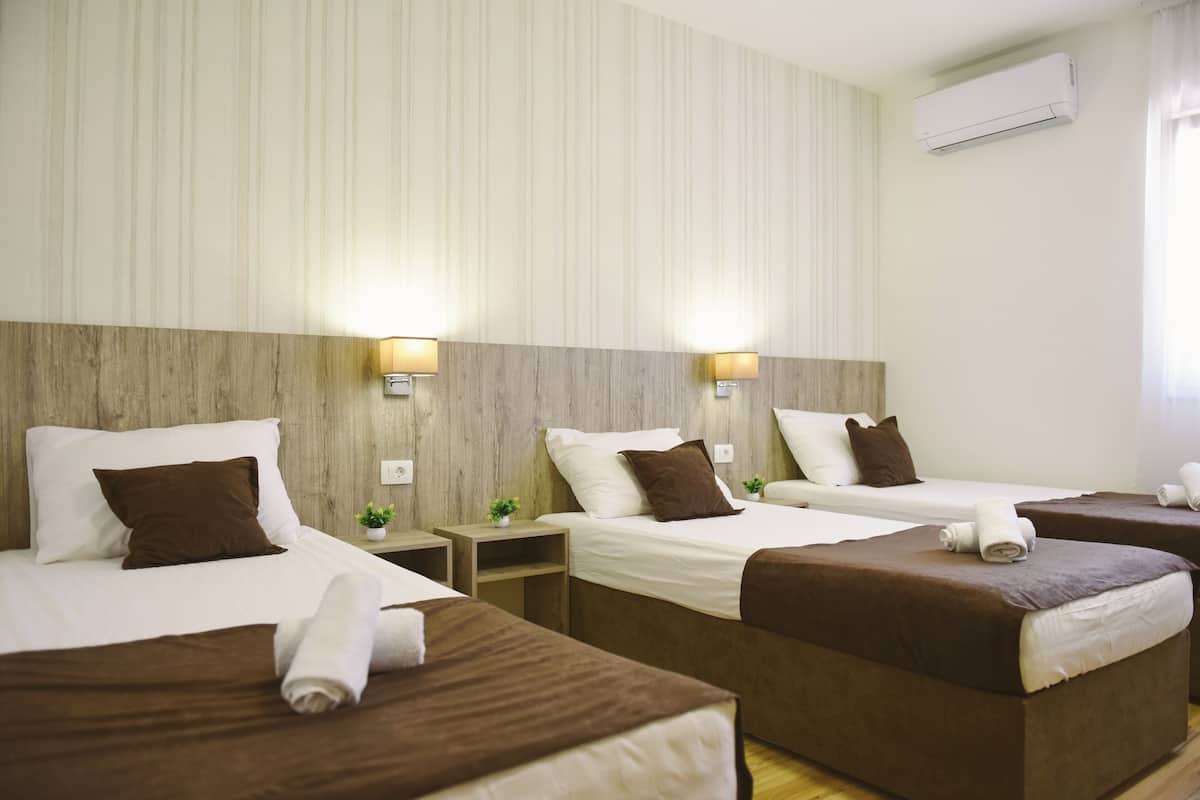 A hotel room with two single beds, a wooden headboard, a small bedside table with a lamp, and an air conditioning unit on the wall.