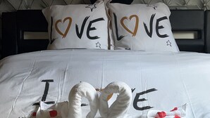 Una cama con cabecera capitonada, dos almohadas con la palabra 'LOVE' escrita y una manta con 'I LOVE THE STAR', además de dos toallas con forma de cisne.