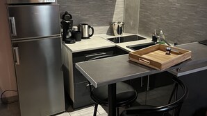 Una cocina compacta con microondas, cafetera y un lavamanos pequeño. Hay una bandeja de madera en la encimera y dos taburetes negros.