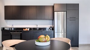 Une cuisine moderne avec des meubles de couleur sombre, un réfrigérateur en acier inoxydable et une table ronde sur laquelle se trouve un saladier rempli de fruits.