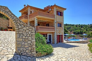 Un immeuble à plusieurs étages, doté d’une façade en pierre, d’un espace piscine et offrant une vue sur un paysage vallonné.