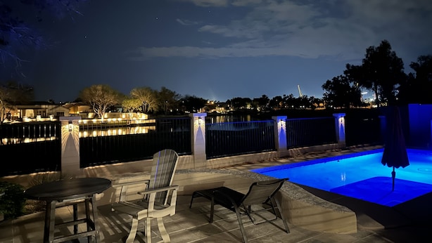 A nighttime outdoor pool area with a view of a city skyline, a covered seating area, and a fence. - Water/Golf Course Backyard | Heated Pool Included in Price | Modern 3 bedroom (Chandler)