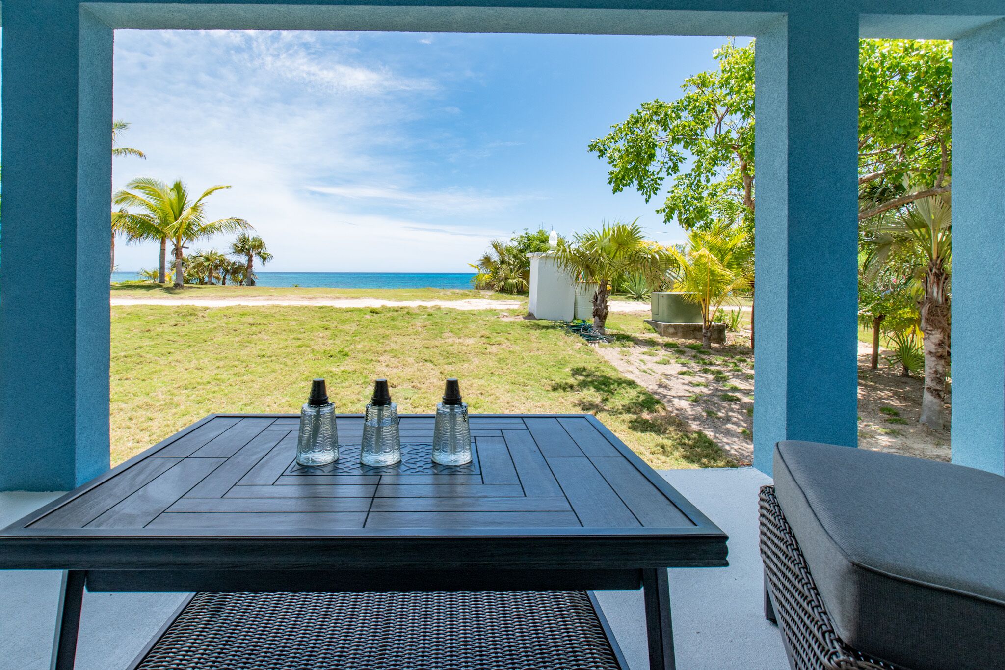 Una mesa con tres botellas de agua y vista a una playa con palmeras y cielo despejado.