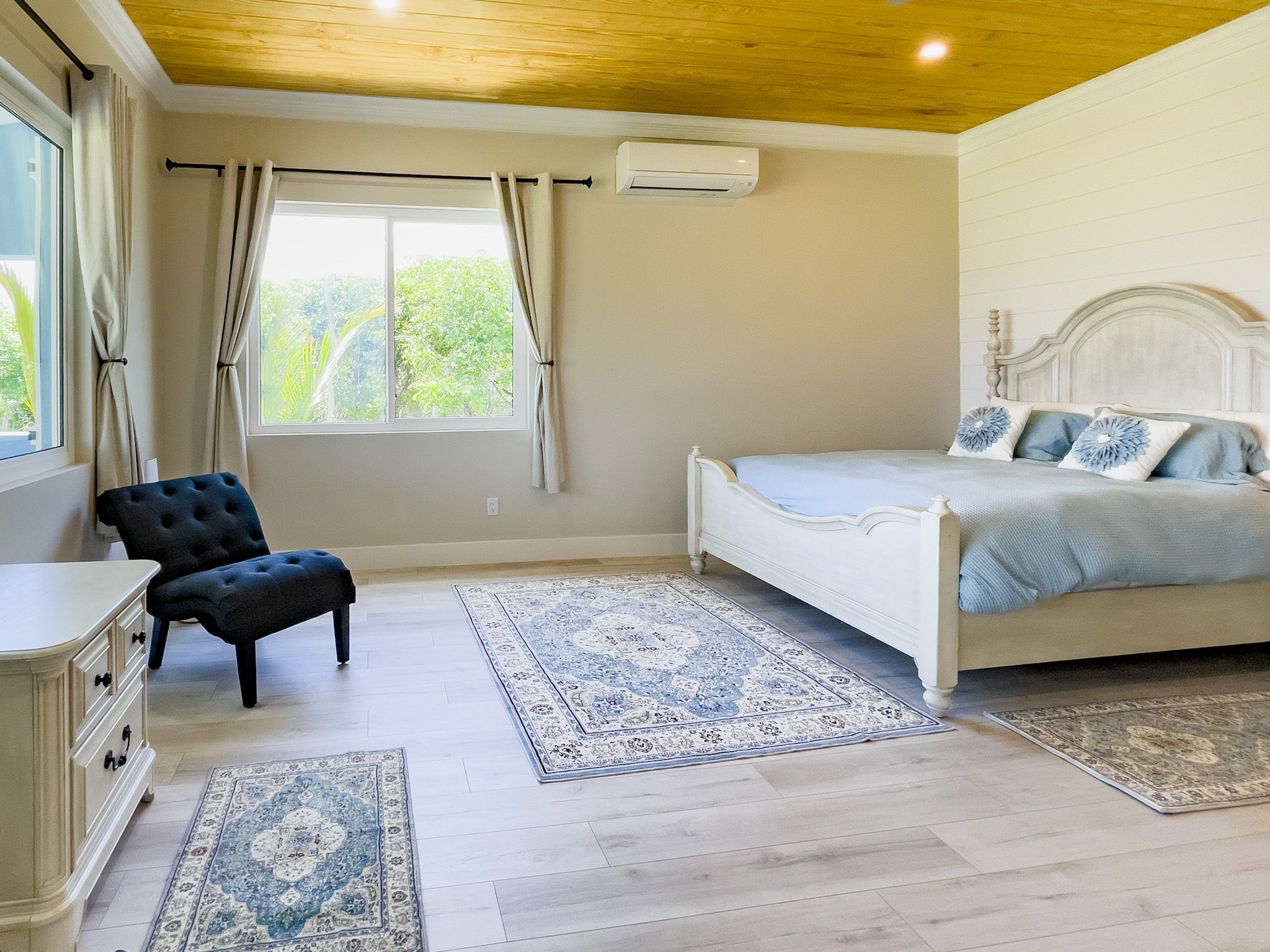 A bedroom with a bed, a chair, a dresser, and a window with curtains.