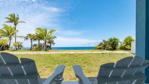 Zwei weiße Adirondack-Stühle, die auf einen Strand mit Palmen und blauem Himmel blicken.