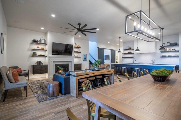 Un grand espace de vie comprenant un coin salon avec cheminée, une table à manger et un coin cuisine avec des tabourets de bar.