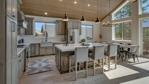 A modern kitchen with wooden cabinets, a central island, pendant lights, and large windows. - Streams and Dreams - TLUXP (Truckee)