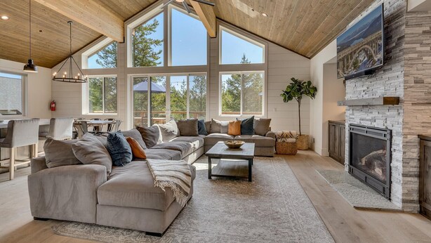 A spacious living room with a large sectional sofa, a fireplace, and a dining area with a view of the outdoors. - Streams and Dreams - TLUXP (Truckee)