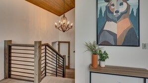 A staircase with a wooden handrail and a chandelier, a framed abstract painting, and a potted plant on a console table. - Streams and Dreams - TLUXP (Truckee)