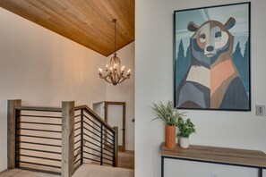 Eine Treppe mit hölzernem Geländer und einem Chandelier, ein gerahmtes abstraktes Gemälde und ein Blumentopf auf einer Konsolentisch.
