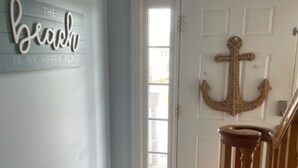 Een hal met een houten vloer, een witte deur met ankerdecoratie, en een bord op de muur waarop staat: 'The beach is my happy place'.