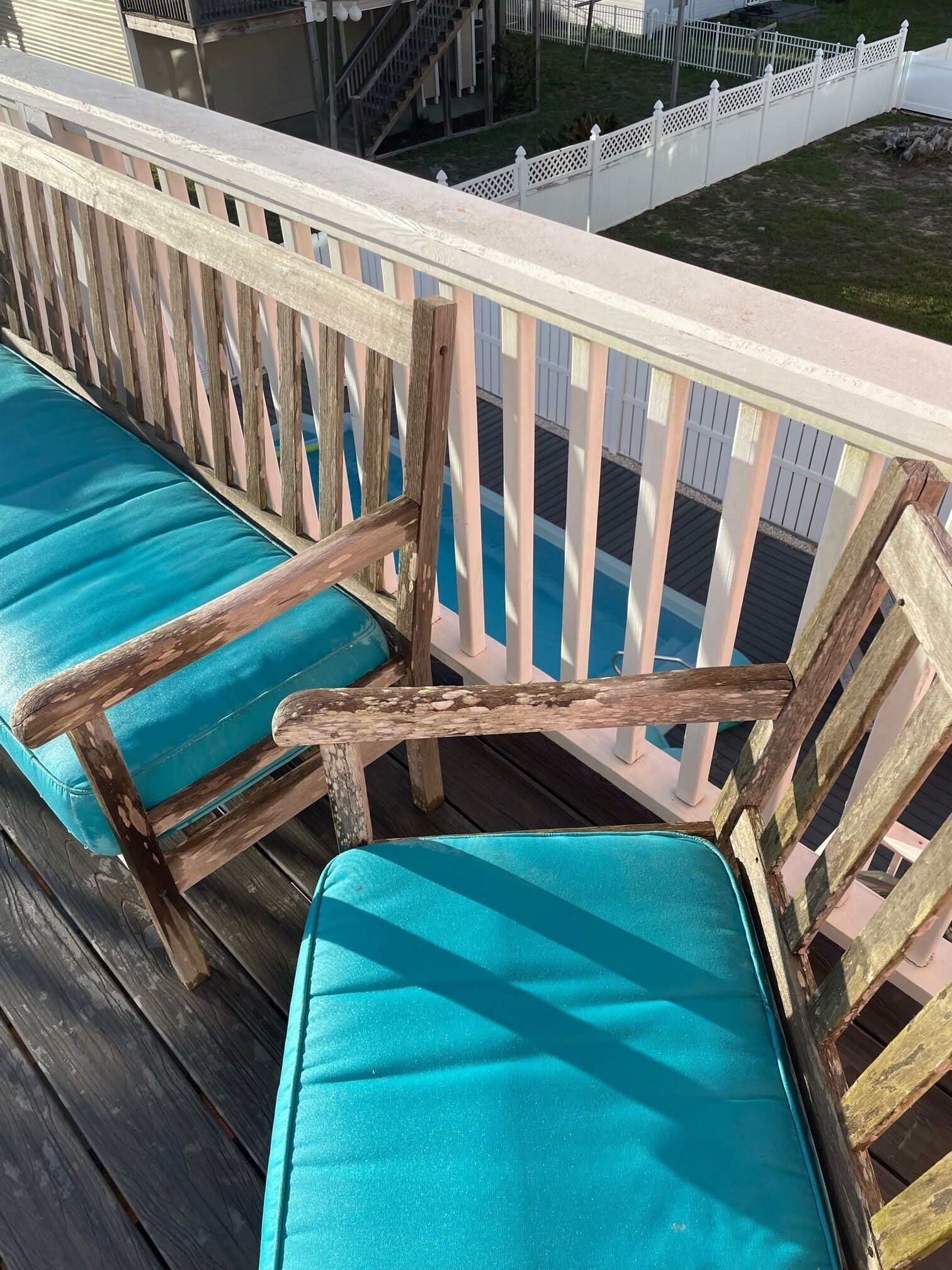 A wooden deck with turquoise cushioned chairs and a white picket fence.