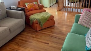 Een ruime woonkamer met een houten vloer, een groene bank, een oranje bank en een grijze bank.