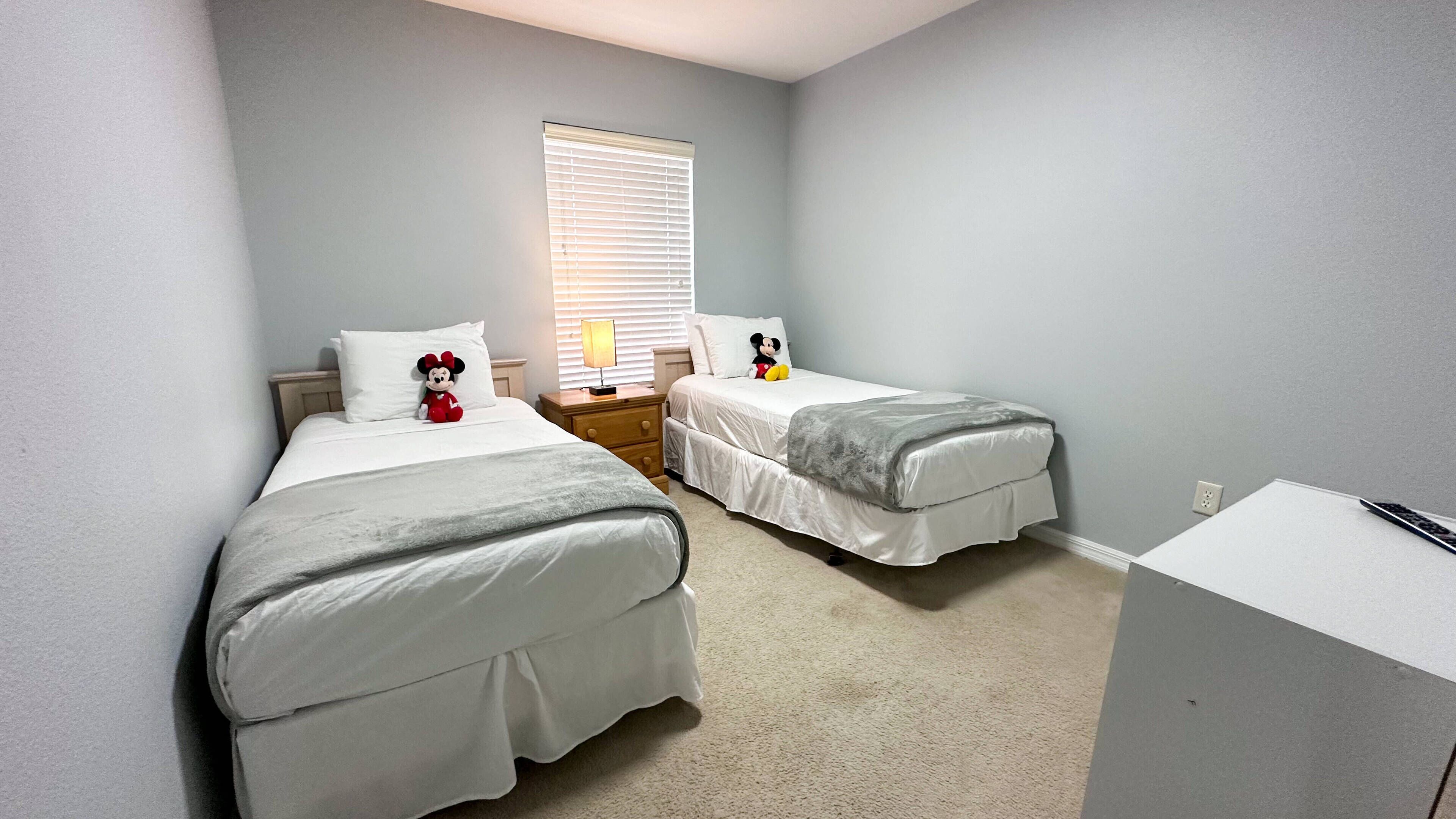 Een slaapkamer met twee bedden, een nachtkastje, een lamp en een Mickey Mouse knuffel.