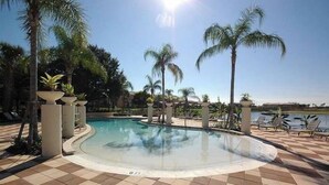 A pool area with a tiled floor, palm trees, and lounge chairs.