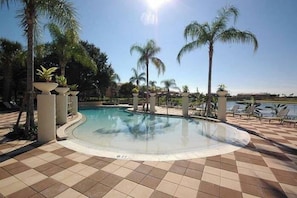 A pool area with a tiled floor, palm trees, and lounge chairs.