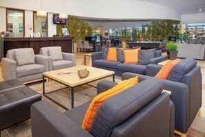 Un moderno vestíbulo de hotel con zonas de estar, una recepción y una piscina.