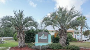 A sign for Villas with a landscaped area featuring palm trees and a truck in the background.
