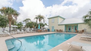 A swimming pool with lounge chairs and umbrellas, a building with teal trim, and palm trees.