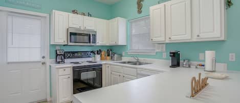 A kitchen with white cabinets, a microwave, a coffee maker, and a sink.