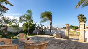 An outdoor patio with wicker furniture and a view of palm trees and a stone wall. - 3156 Villa Andrea House by Barbarhouse (Porto Cesareo)