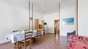 A dining area with a table set for four, a kitchen in the background, and a bed with a patterned bedspread. - 2345 Le Due Torri - Torre Grande by Barbarhouse (Melendugno)