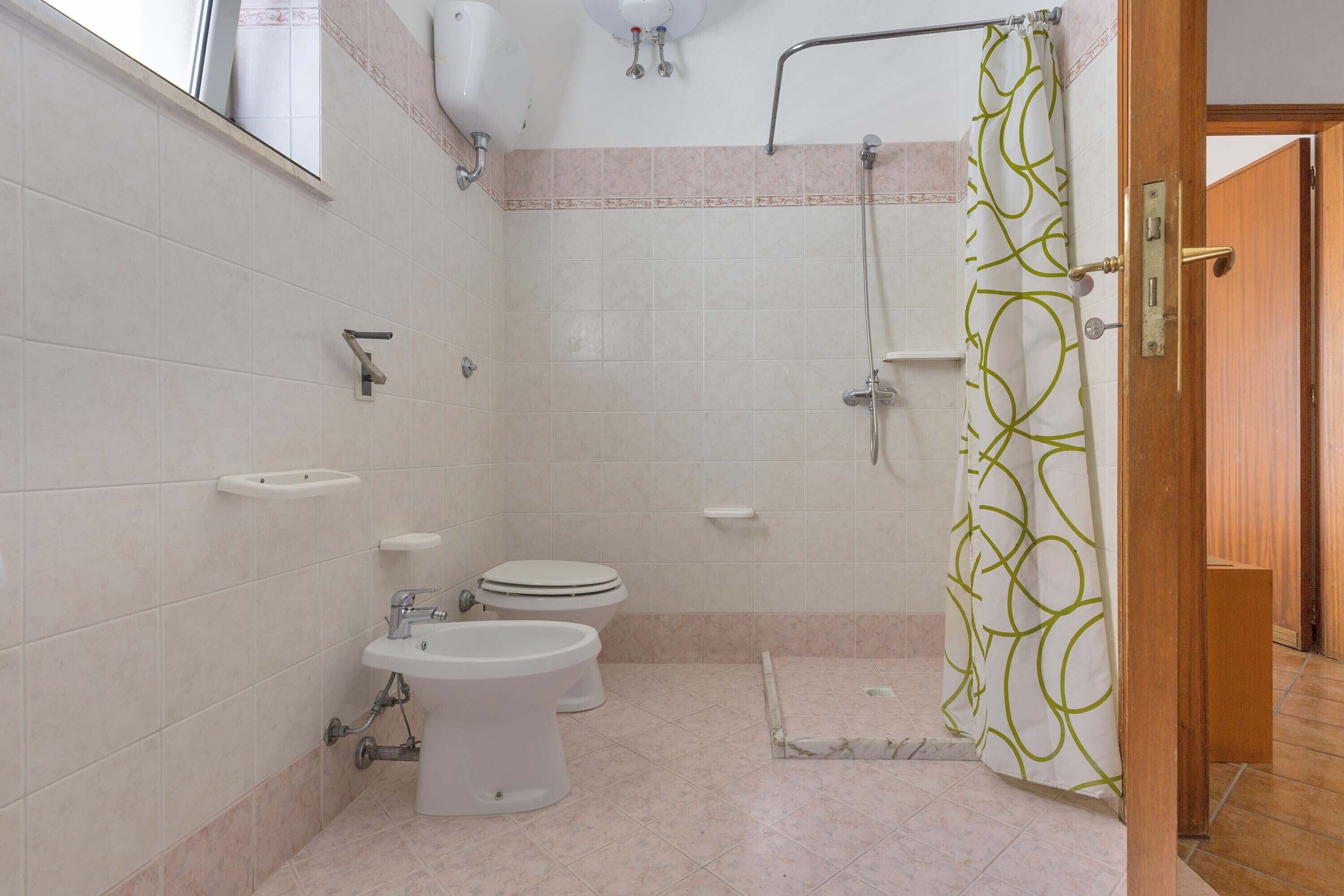 A bathroom with a toilet, bidet, sink, shower, and a curtain with a geometric pattern.