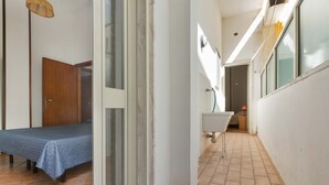 A narrow hallway with a bed on the left, a sink on the right, and a door at the end. - 2345 Le Due Torri - Torre Grande by Barbarhouse (Melendugno)