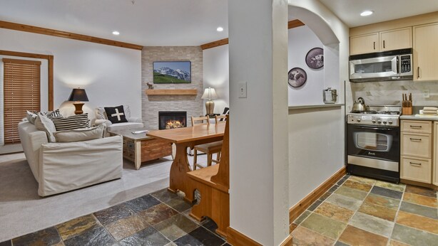 A living room with a sofa, coffee table, and fireplace. There is a dining area with a table and chairs. The kitchen has modern appliances and cabinets. - Family Getaway~pool, Tubing, Skiing, & Ice Castles Villa 1002 1 Bedroom Villa by RedAwning (Midway)