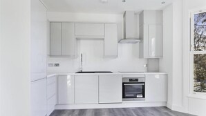 Een moderne keuken met witte kastjes, een inbouwoven en een raam met uitzicht op bomen.
